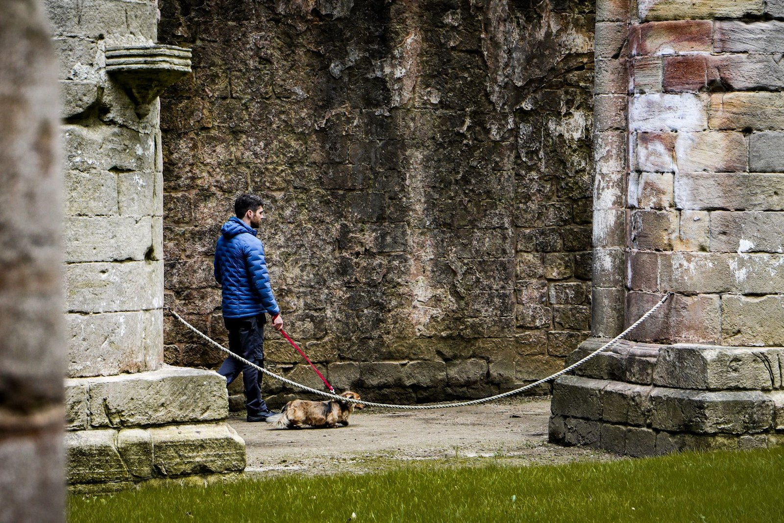 A man walks his dog near ancient ruins, showcasing historical architecture.